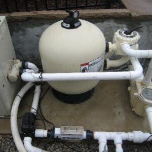Pool equipment on a concrete pad including a round tan sand filter, pump, and PVC piping.